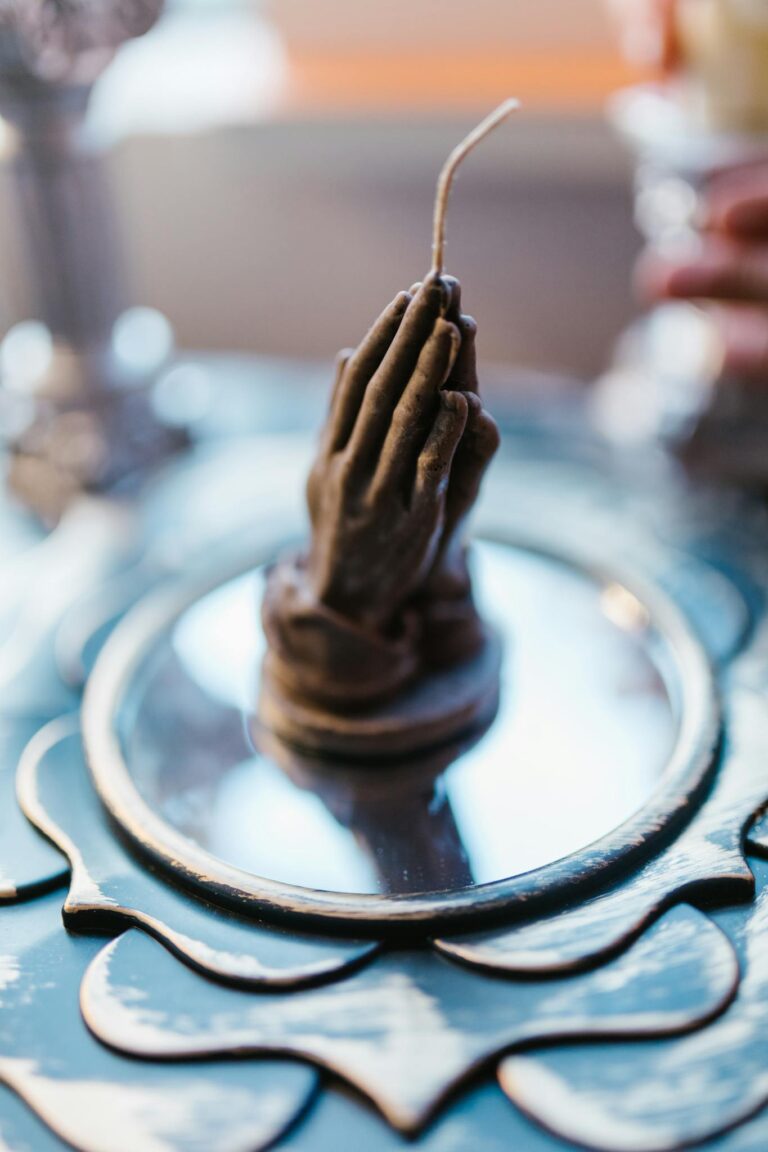 Handcrafted candle shaped like praying hands on a reflective surface, perfect for inspiration or spiritual ambiance.